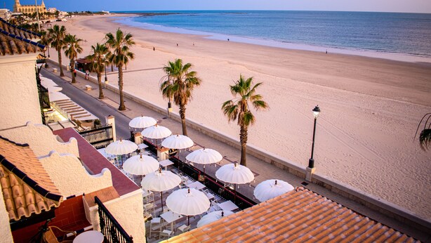 Un hotel frente a la playa con asientos al aire libre y palmeras.