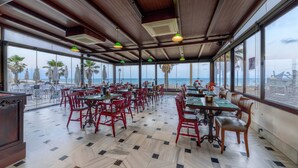Un comedor amplio con ventanas grandes que dan a la playa, con sillas y mesas rojas.