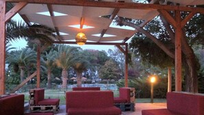 Un espace extérieur aménagé avec des canapés et des tables aux coussins rouges, des poutres en bois et un luminaire suspendu.