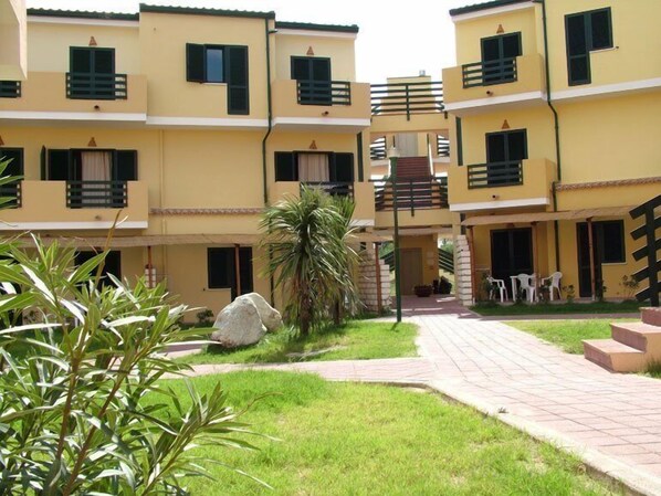 A multi-story building with balconies, a central staircase, and a paved courtyard with grass and plants. - Villaggio Santandrea Resort (Sant'Andrea Apostolo dello Ionio)