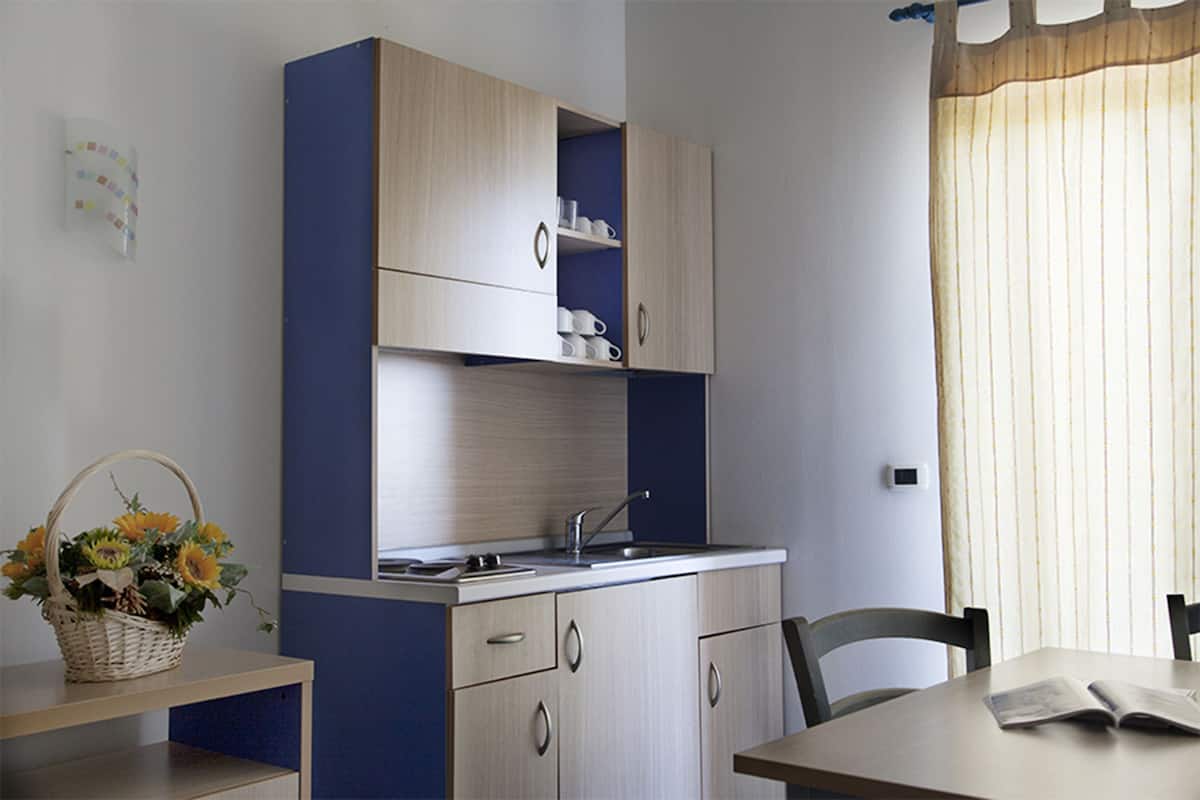 Een compact keukenhoekje met een spoelbak, kastjes, en een eethoek met een tafel en stoelen.
