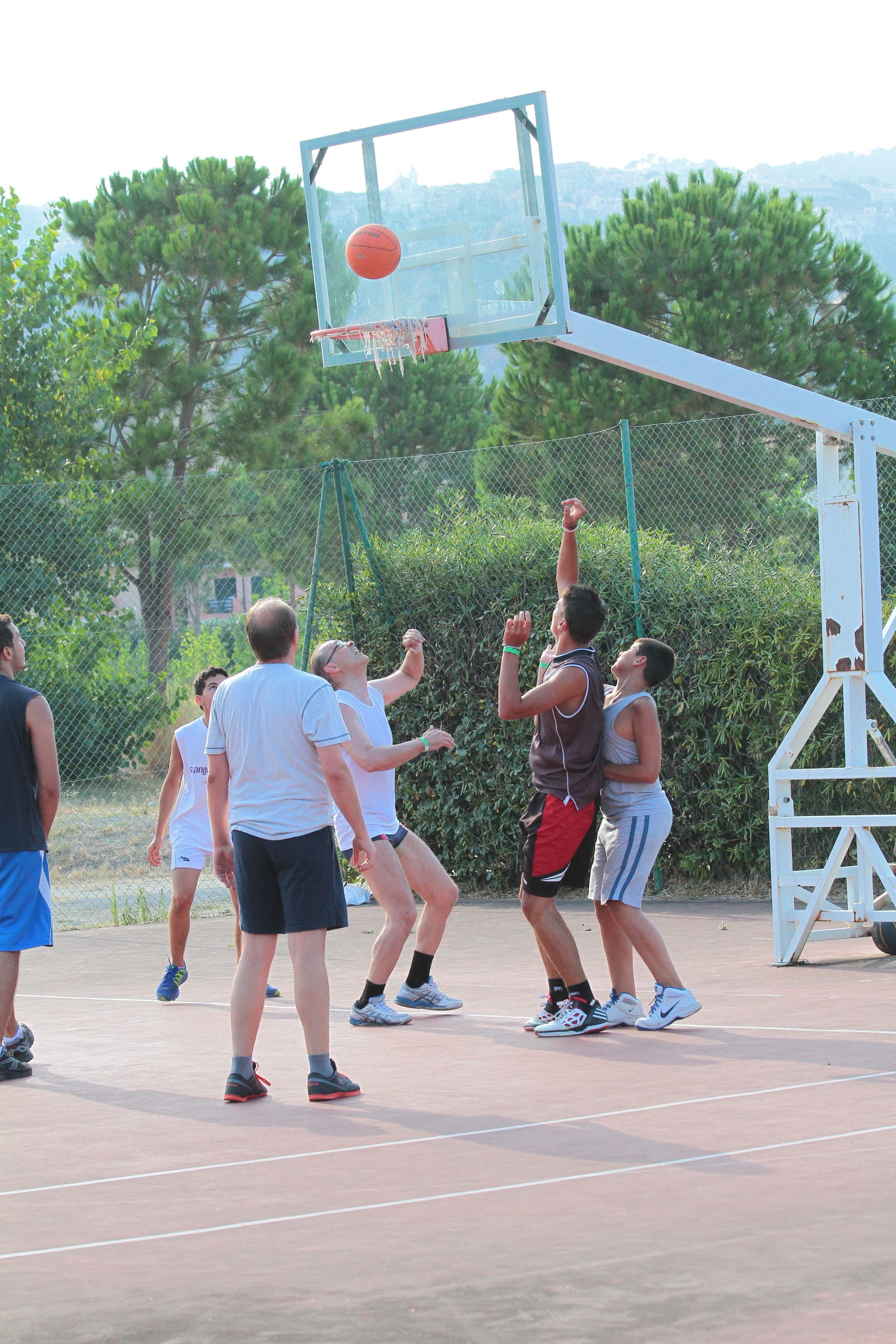 A basketball court with players in motion, a basketball hoop, and a chain-link fence.