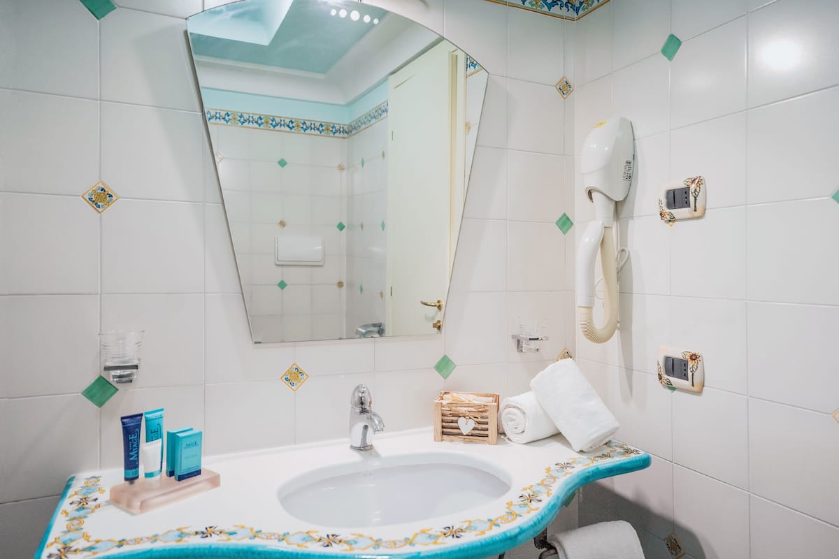 A bathroom with a sink, mirror, hairdryer, and toiletries.