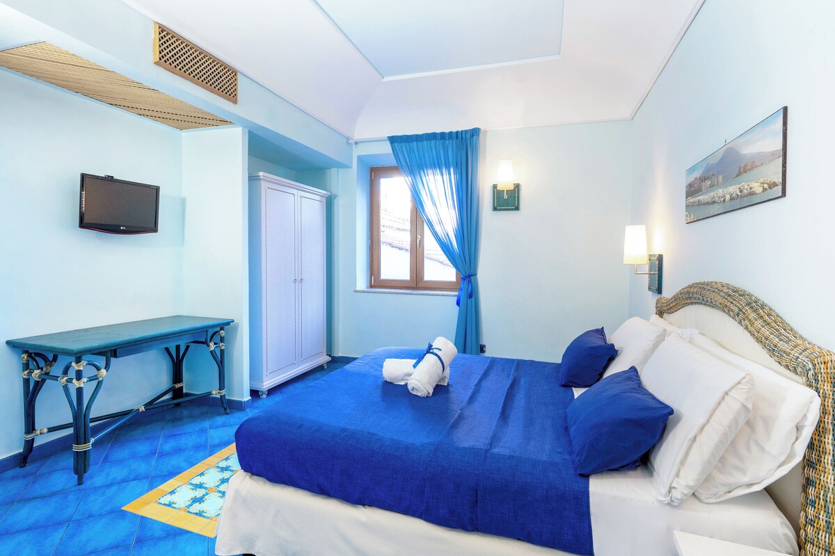 A hotel room with a bed, a desk, a television, and a window with curtains.