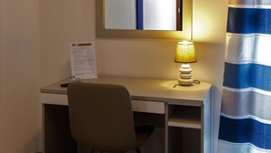 Habitación de hotel con escritorio, silla, aire acondicionado y cortina a rayas.