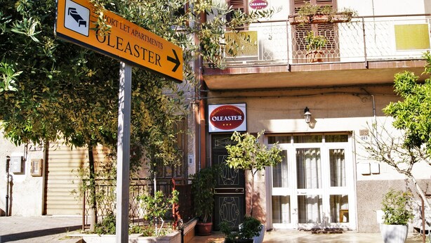 Un edificio con un letrero que dice 'Oleaster' apartamentos, una entrada con portón y plantas en macetas.