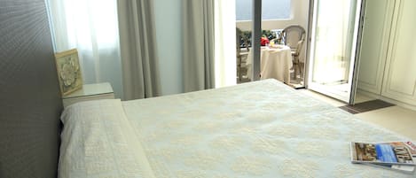 Une chambre d’hôtel avec un grand lit, une petite table avec une chaise, et une vue sur la mer grâce à une porte coulissante.
