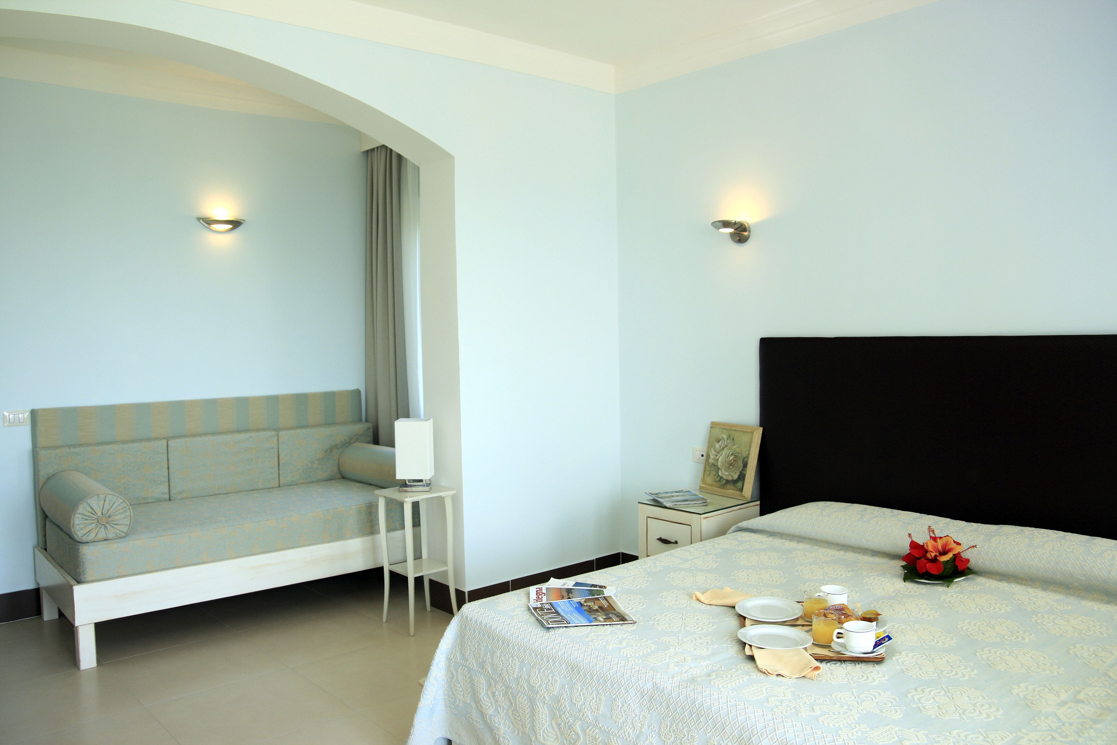 A hotel room with a bed, a sofa, a small table, and a nightstand.