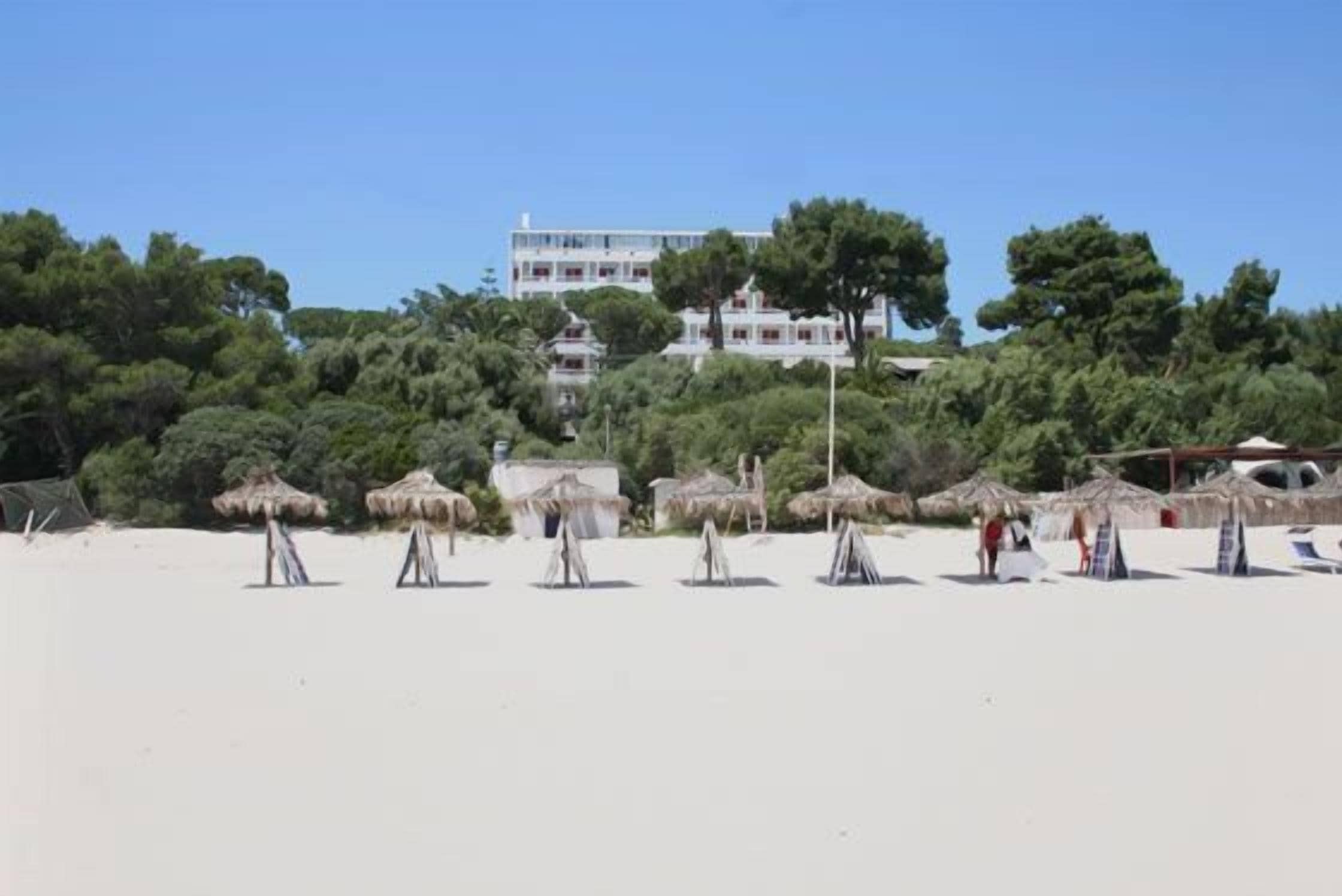 A beach with thatched umbrellas and a building in the background.