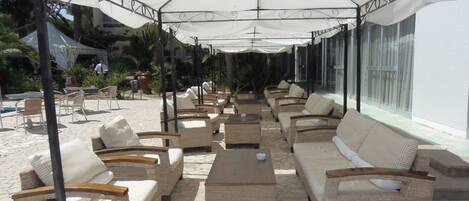 An outdoor seating area with wicker furniture and umbrellas, overlooking a pool and greenery.