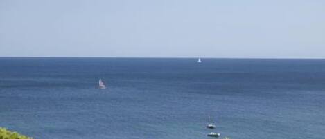 A coastal view with a clear sky, a sailboat, and a small motorboat in the distance.