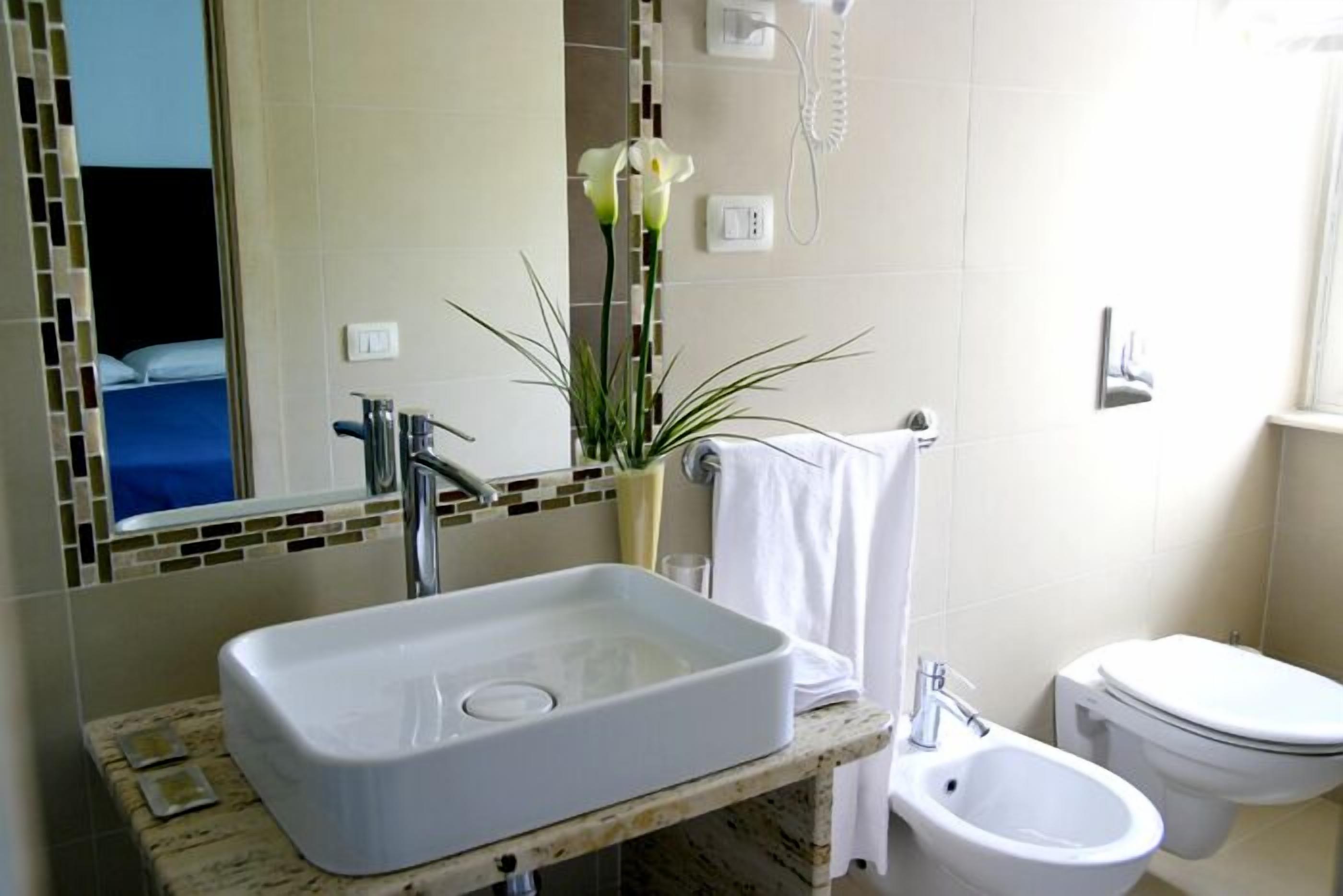 Een badkamer met een rechthoekig wastafelmeubel, een bidet, een toilet en een spiegel met een mozaïekachtergrond.
