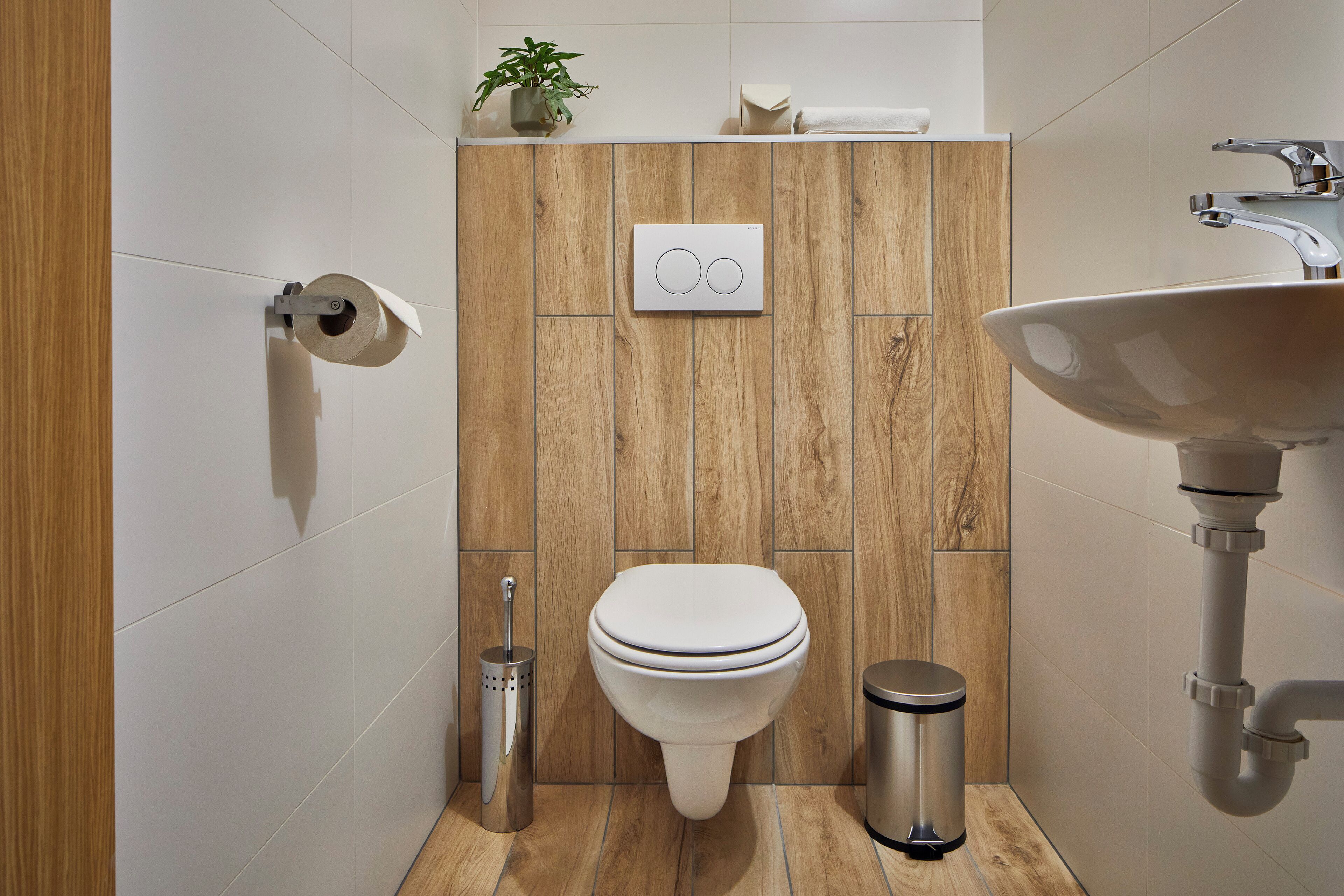 Een moderne badkamer met een wand van houtpanelen, een toilet, een wastafel en een toiletborstel.