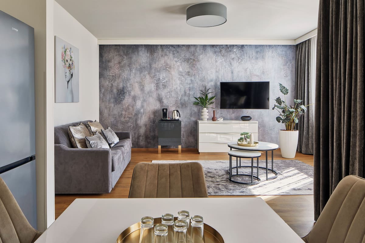 Ein modernes Wohnzimmer mit grauem Sofa, einem Esstisch mit Gläsern, einem Fernseher an der Wand und einer strukturierten grauen Wand.