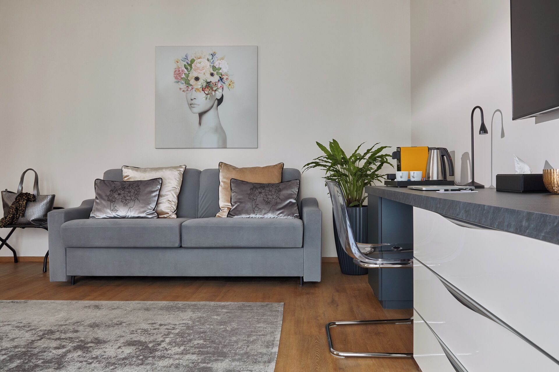 Ein modernes Wohnzimmer mit einem grauen Sofa, einer Kaffeemaschine und einer Pflanze.