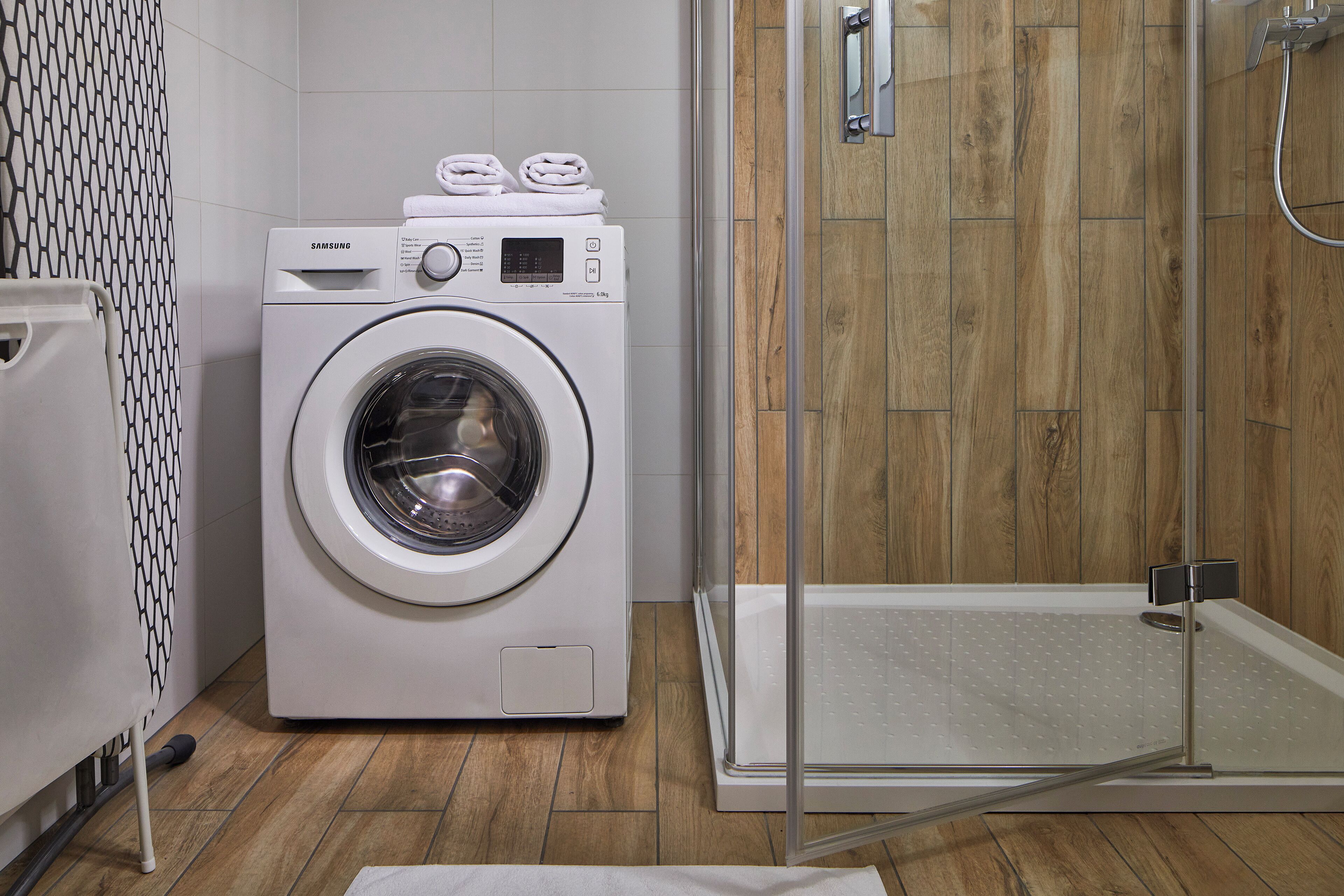Un baño moderno con lavadora incorporada, cabina de ducha de vidrio y suelo de madera.
