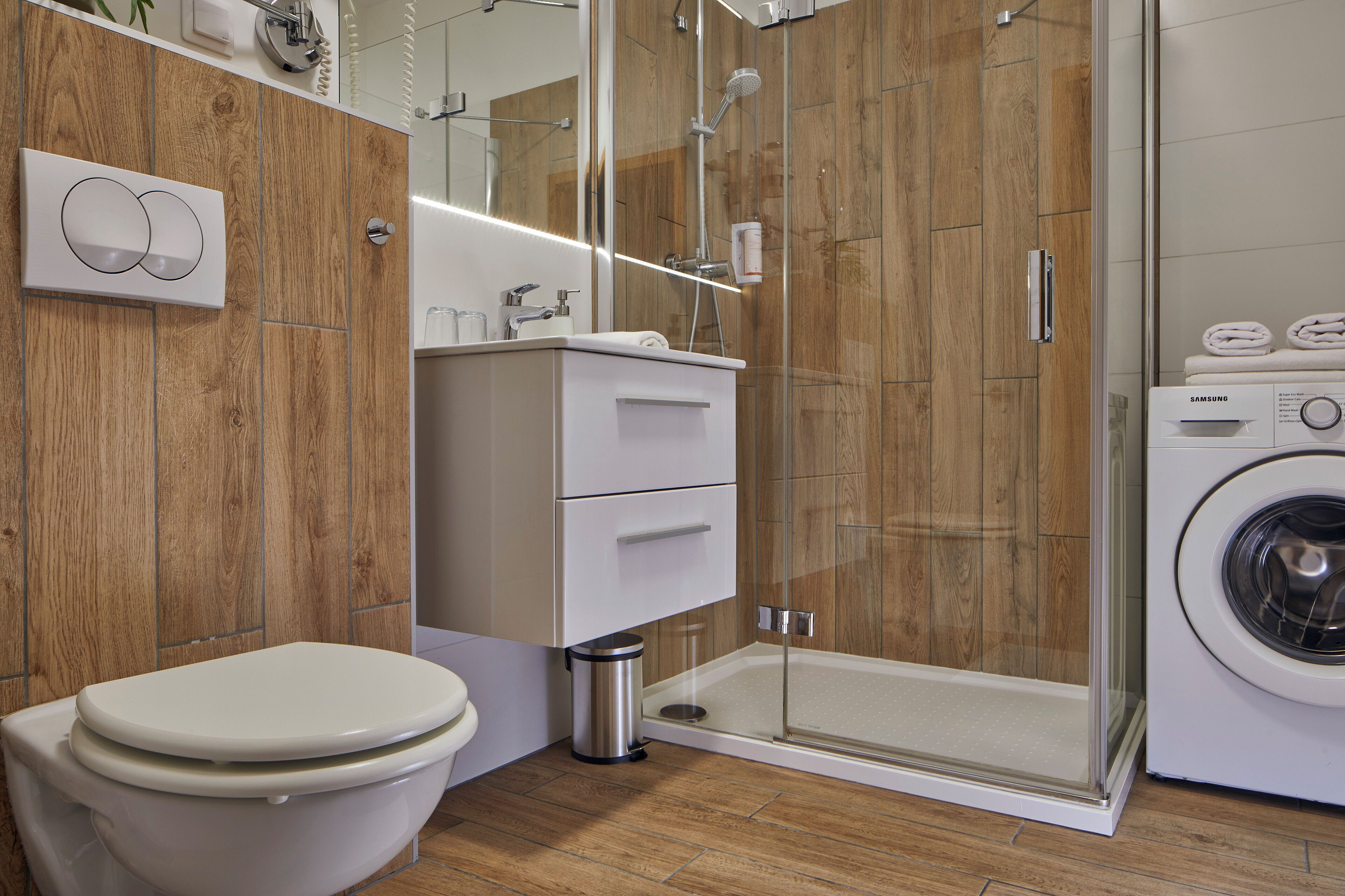 Une salle de bain moderne équipée de toilettes, d’un lavabo, d’un miroir, d’une douche à parois de verre et d’un lave-linge.