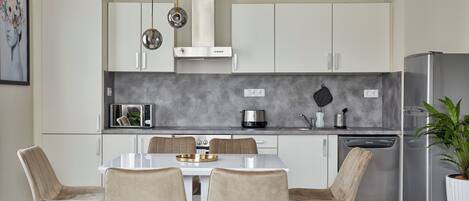 A modern kitchen with white cabinets, a stainless steel refrigerator, and a dining table with four chairs.
