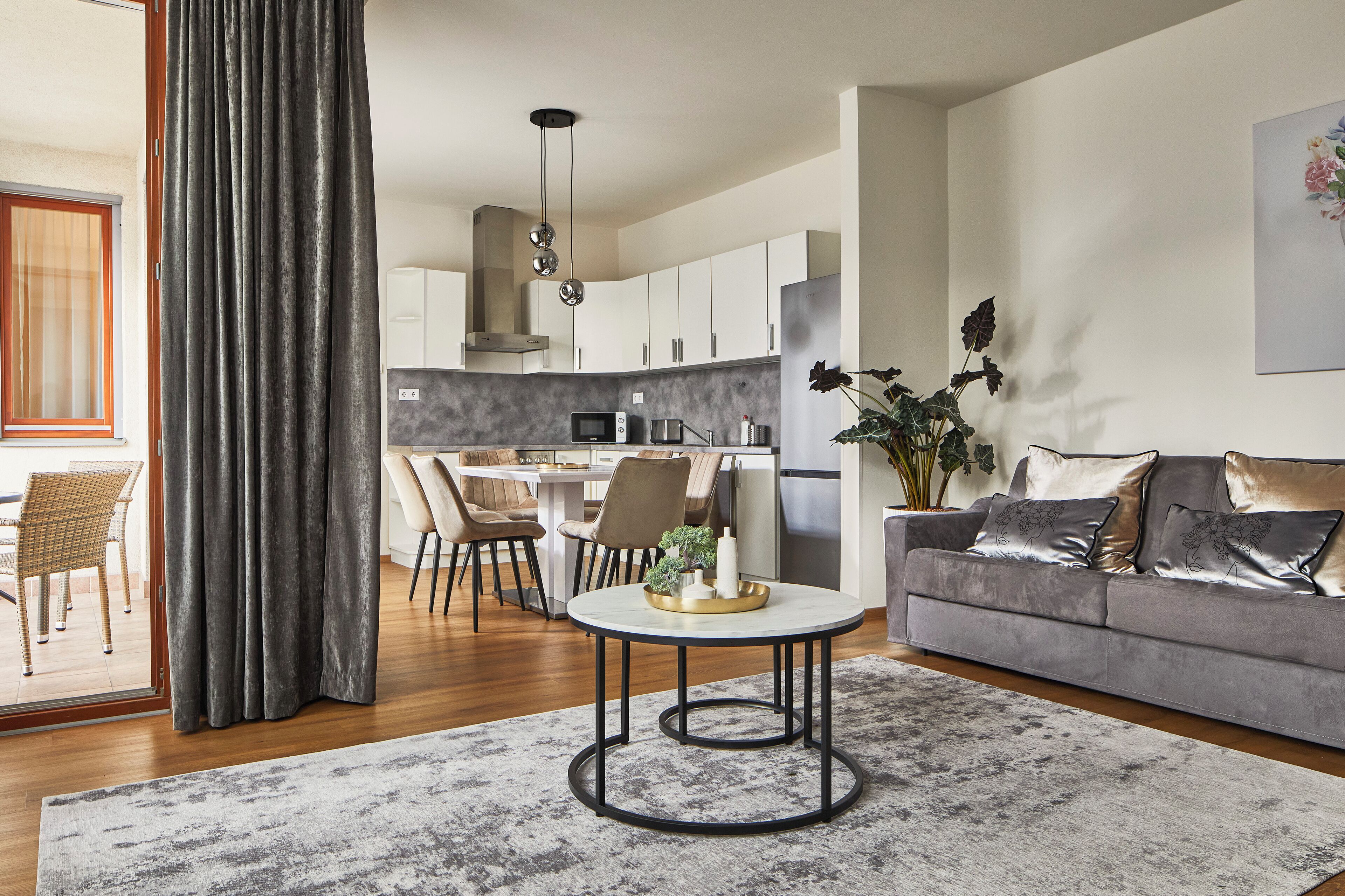 A modern living room with a grey sofa, a round coffee table, and a dining area with a white table and chairs.