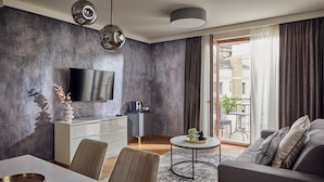 A modern living room with a flat-screen TV, a dining area with a white table, and a grey sofa.