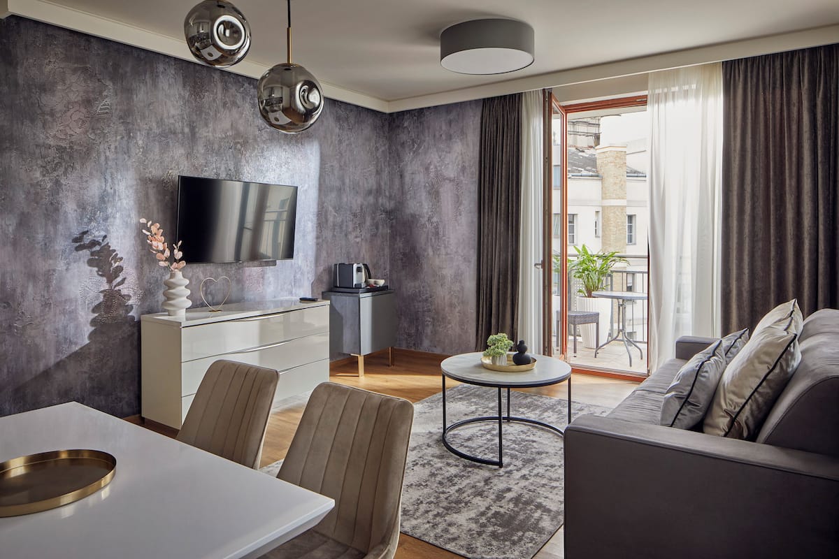 Ein modernes Wohnzimmer mit einem Flachbildfernseher, einem Essbereich mit einem weißen Tisch und einem grauen Sofa.