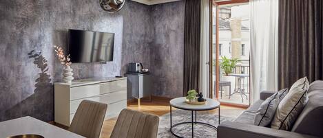 A modern living room with a flat-screen TV, a dining area with a white table, and a grey sofa.