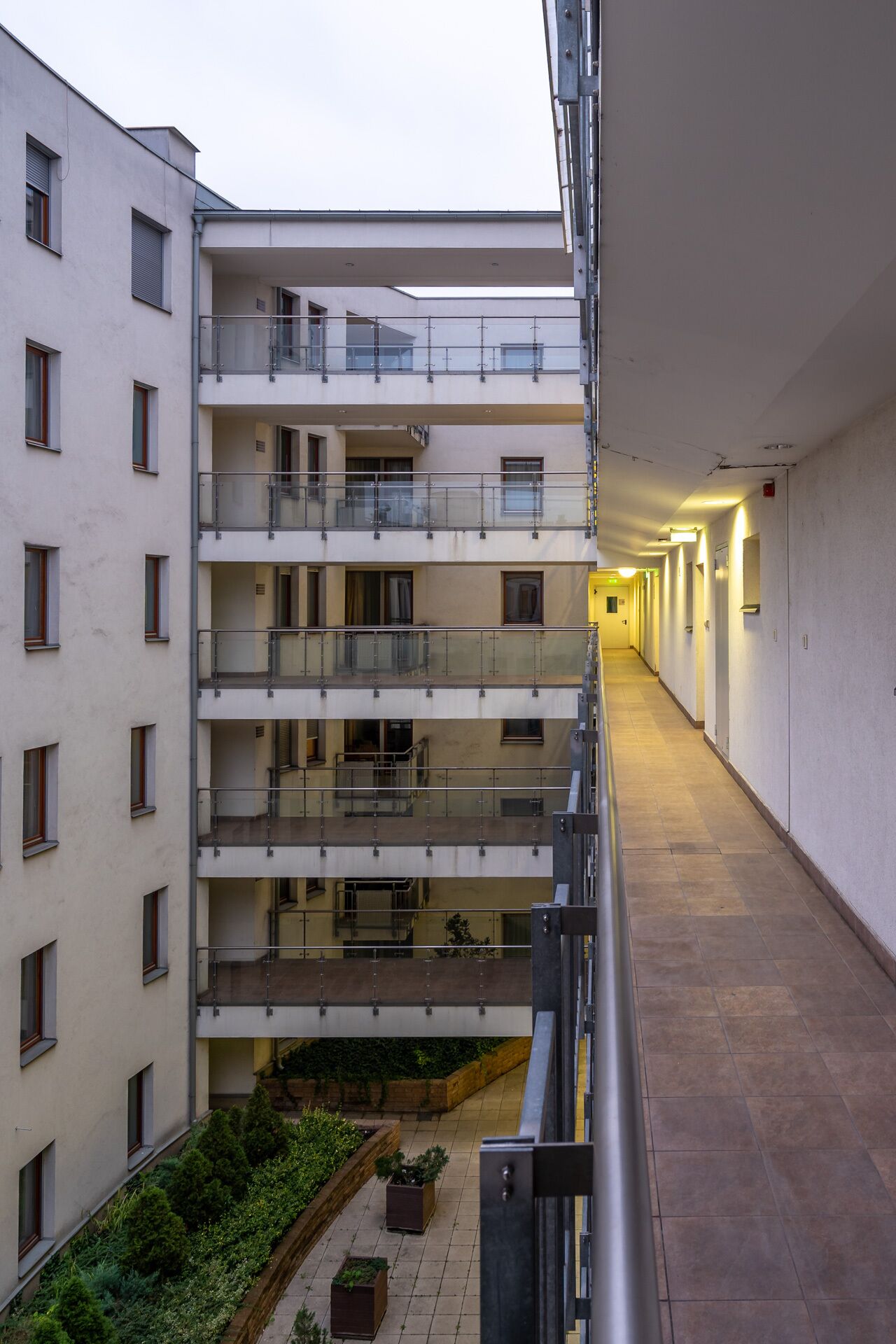 A multi-story residential building with balconies, a covered walkway, and a small garden area.