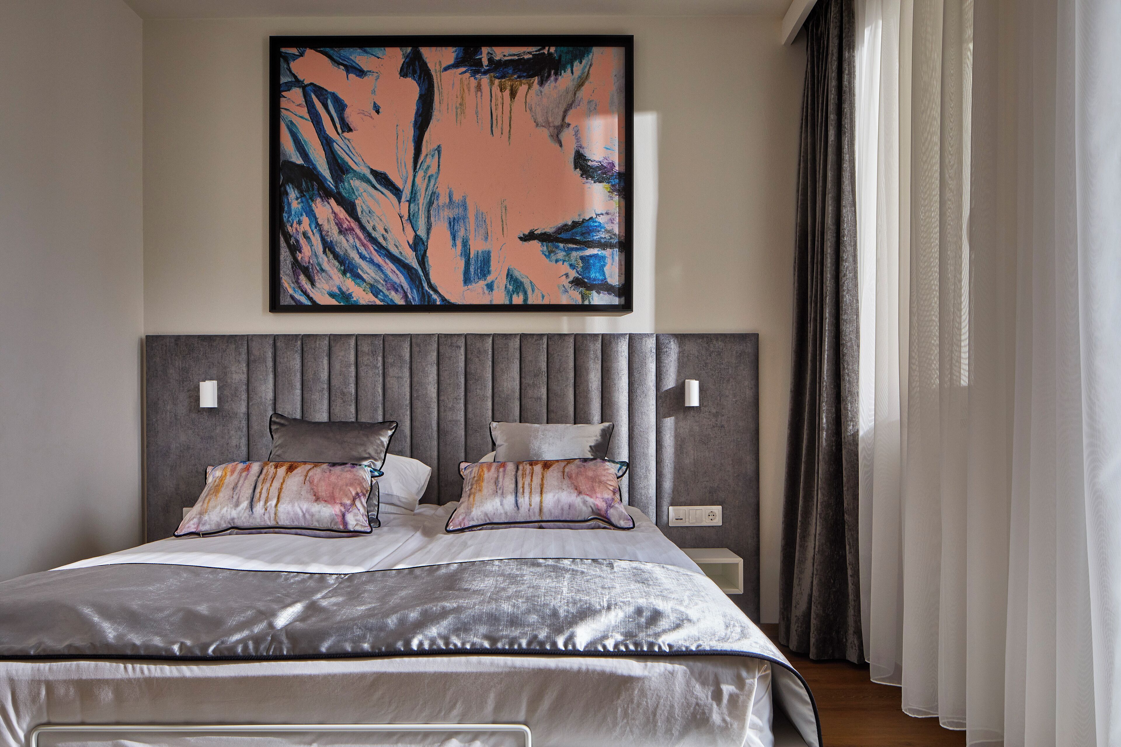 A modern bedroom with a large bed, a headboard with vertical slats, and a large abstract painting above the bed.