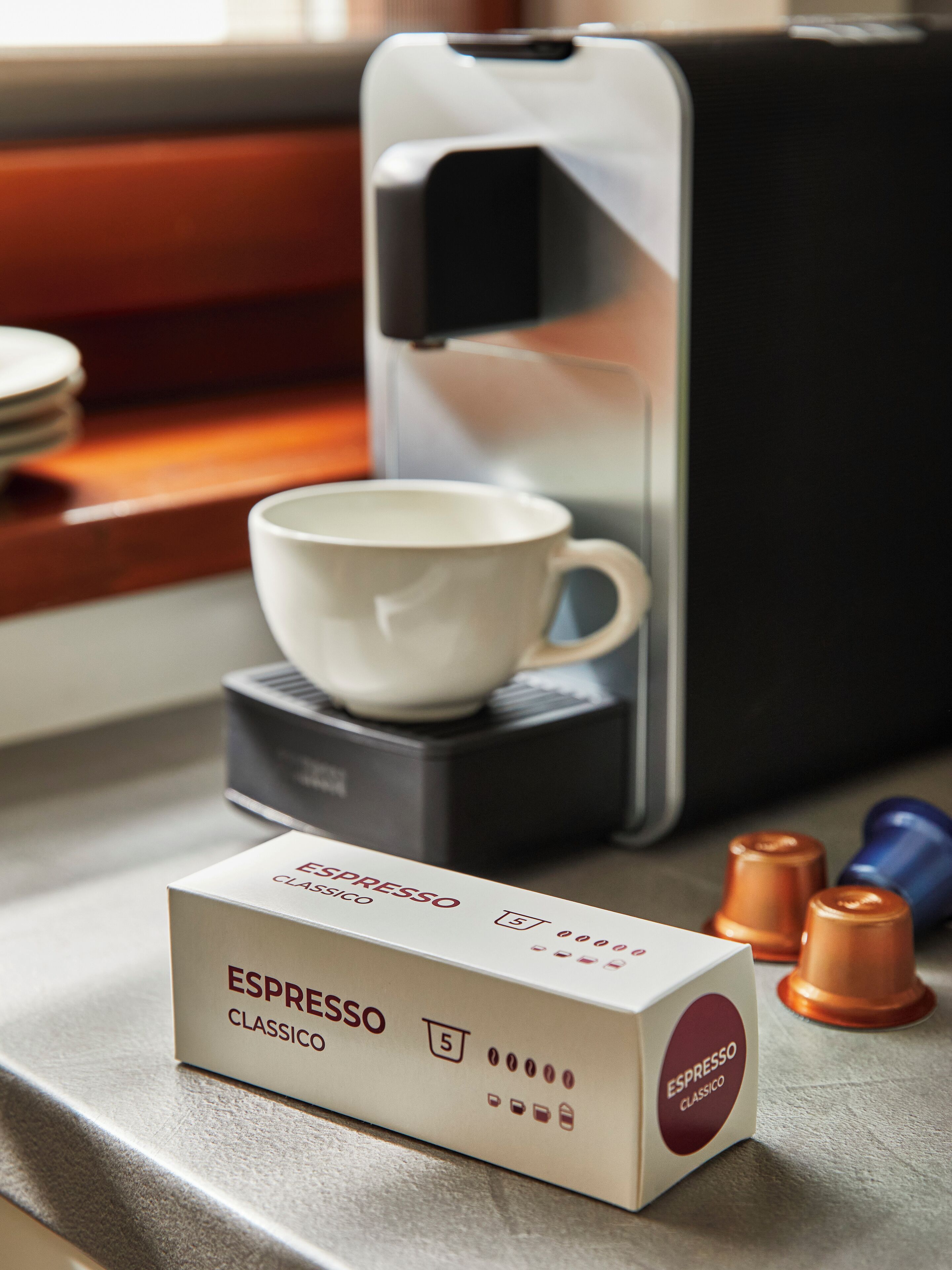 Une machine à café, une tasse et une boîte étiquetée « ESPRESSO CLASSICO » sur un plan de travail.