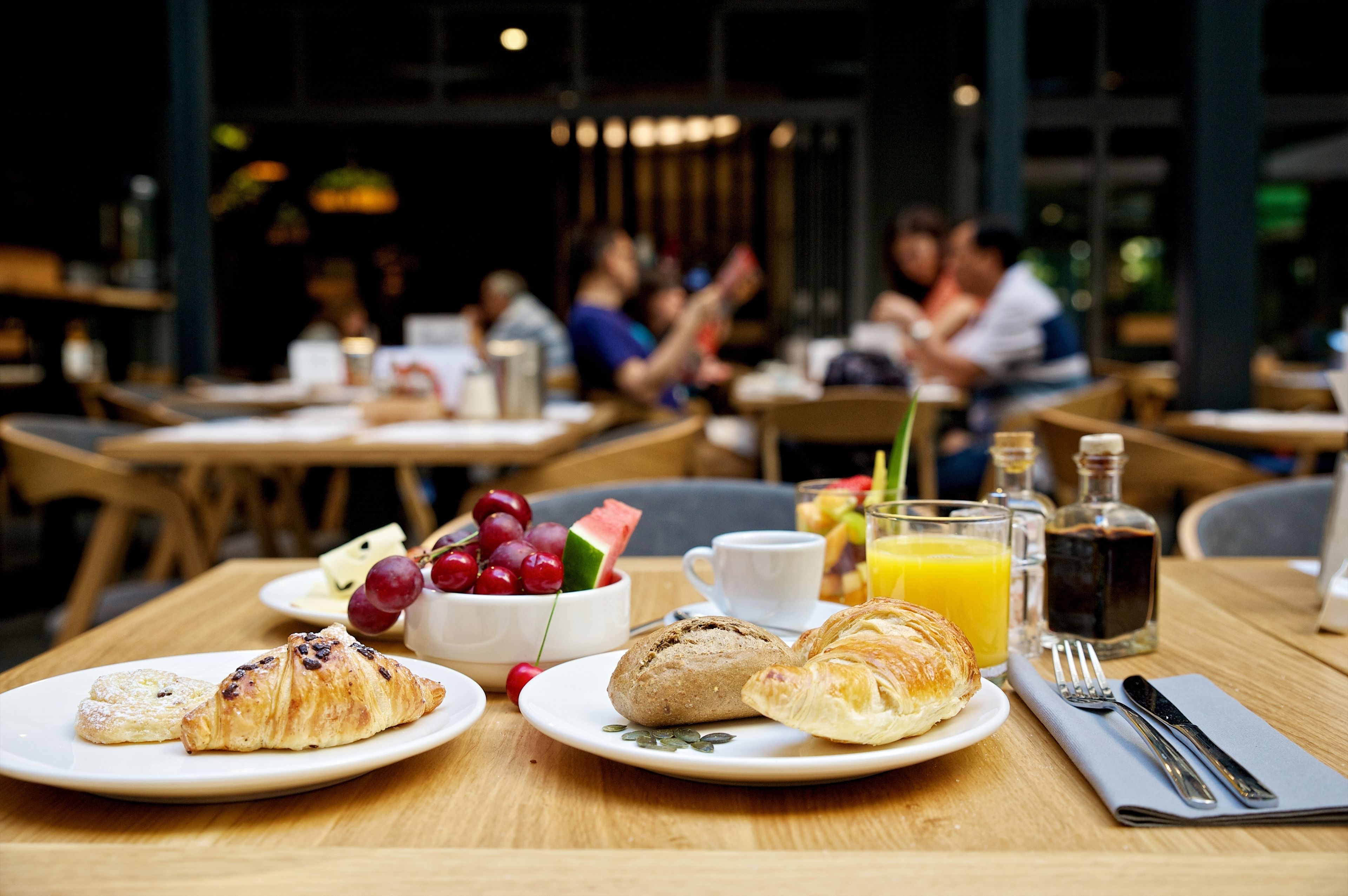 A dining table with croissants, fruit, and juice, set in a restaurant with other tables and chairs in the background.