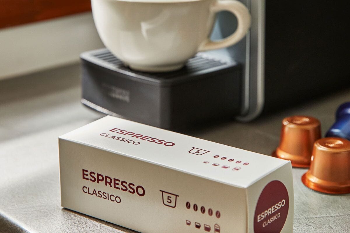 Una confezione di cialde per caffè espresso con l'etichetta 'ESPRESSO CLASSICO', sullo sfondo una macchina da caffè ed due tazzine.