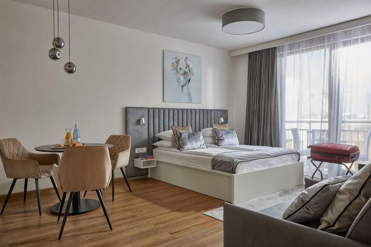 A modern hotel room with a bed, a dining table, and a sofa.