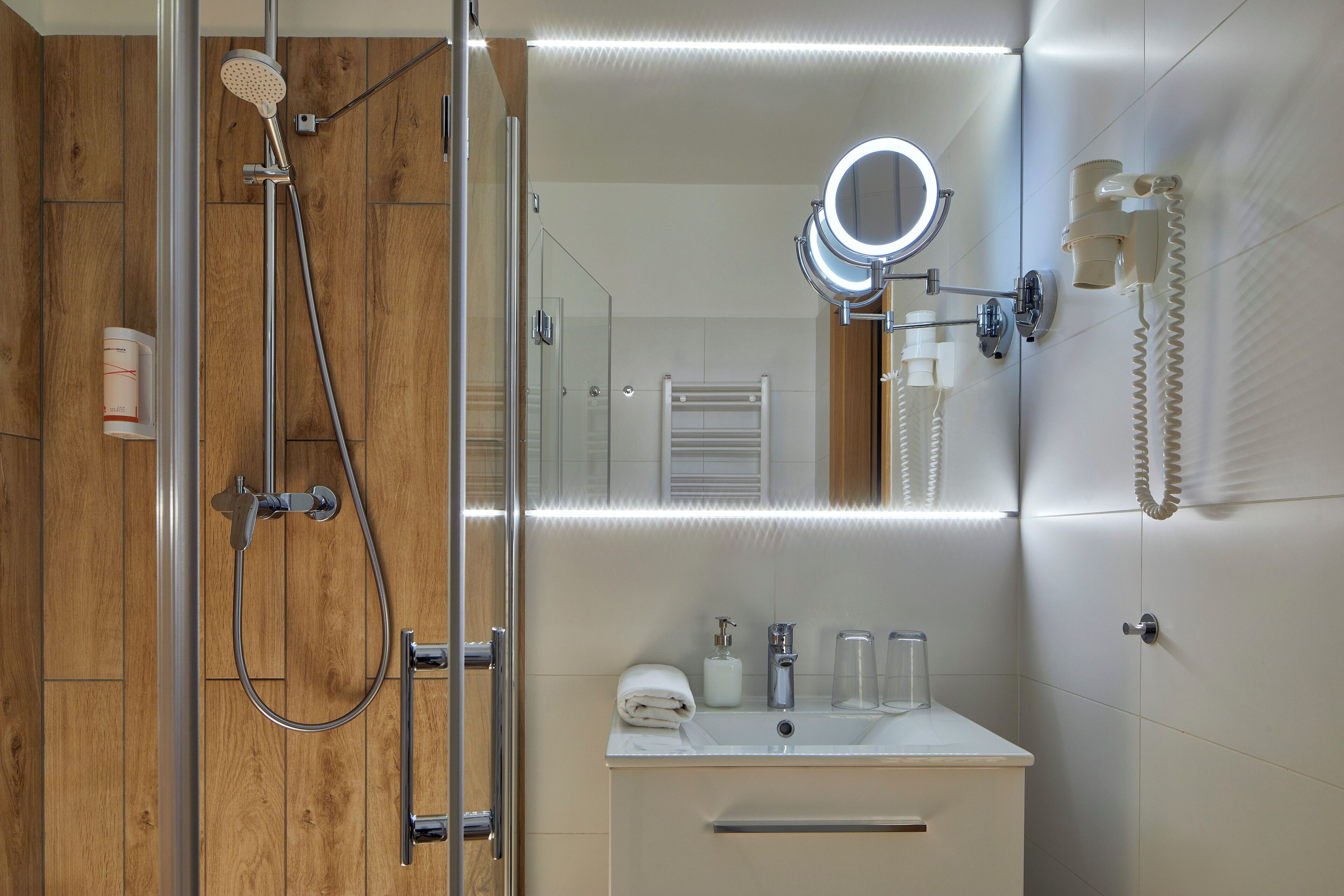Un baño moderno con ducha envuelta en vidrio, tocador con espejo y secador de pelo montado en la pared.
