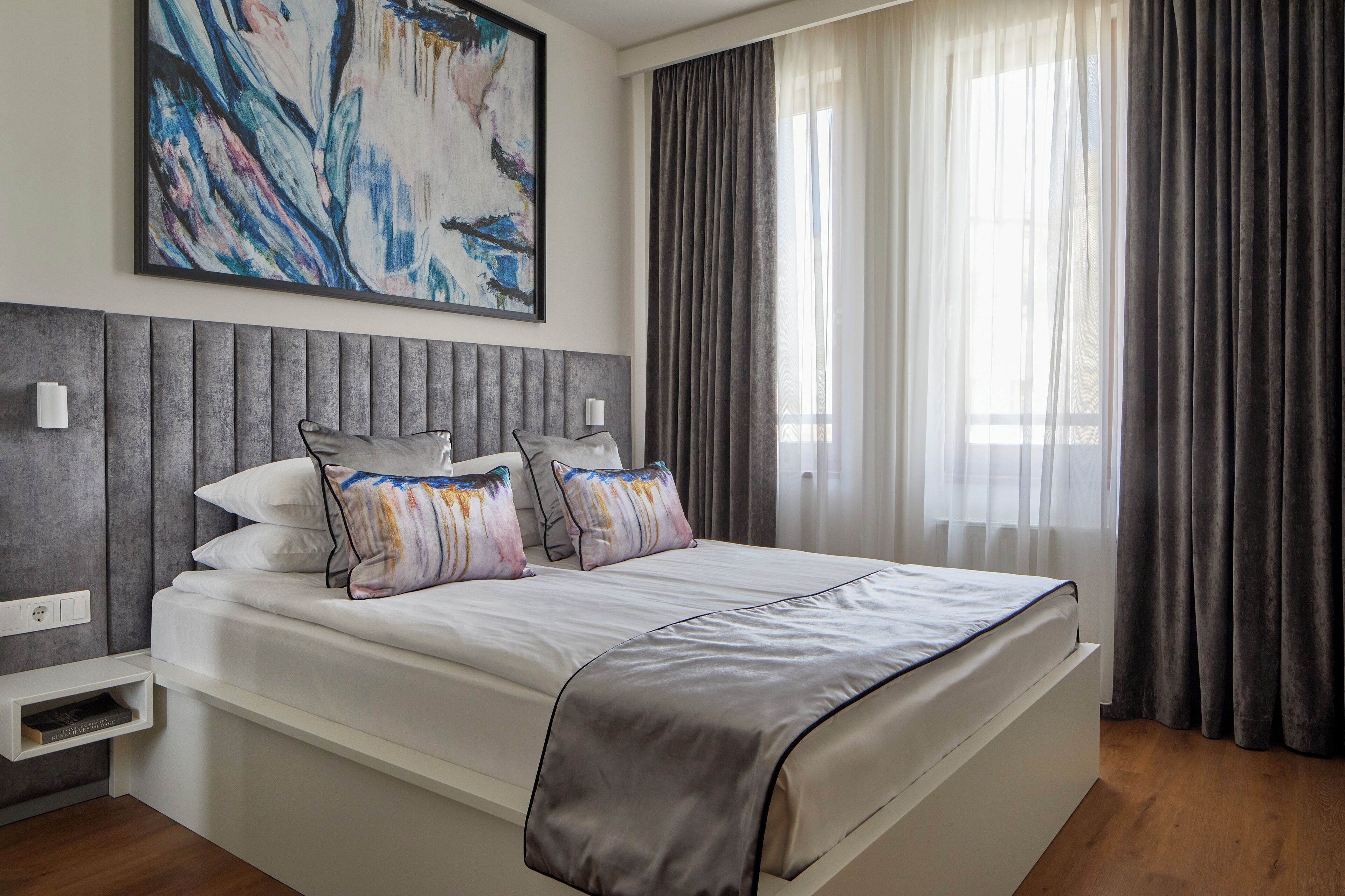 Quarto moderno com cama grande, cabeceira cinza e uma pintura na parede.