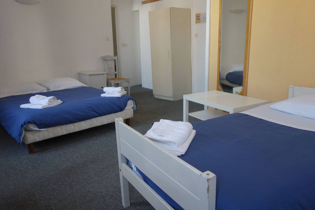 Une chambre d’hôtel avec deux lits, chacun recouvert d’une courtepointe bleue et doté de draps blancs, une petite table de chevet et une armoire.