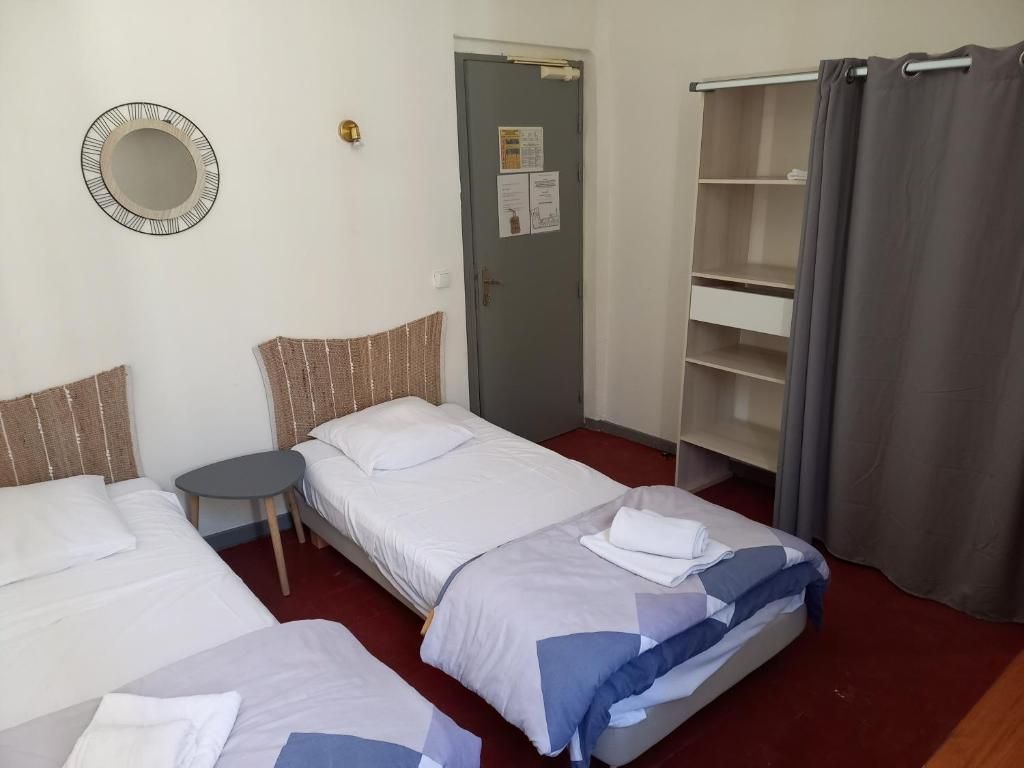 A hotel room with two beds, a small table, a wardrobe, and a door with a bulletin board.