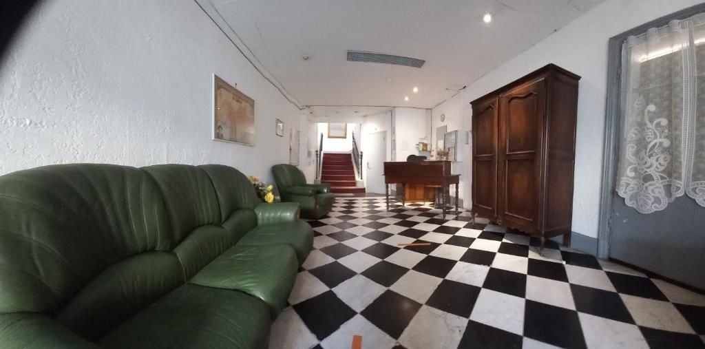 A room with a checkered floor, a green sofa, a wooden cabinet, and a staircase leading to another area.