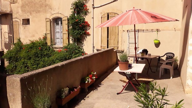 Eine kleine Terrasse im Freien mit Tisch, Stühlen, einem Blumentopf und einem roten Sonnenschirm.