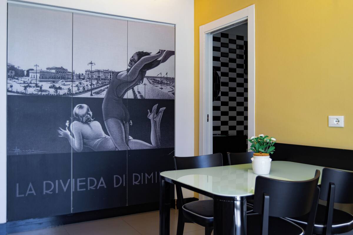 Interior de restaurante com um mural, uma mesa, cadeiras e uma planta em vaso.