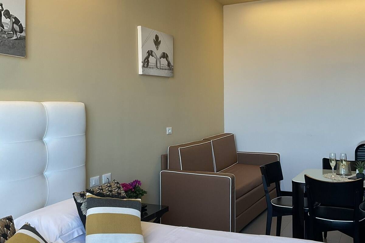 Quarto de hotel com uma cama grande, um sofá marrom, uma mesa de jantar com cadeiras e obras de arte nas paredes.