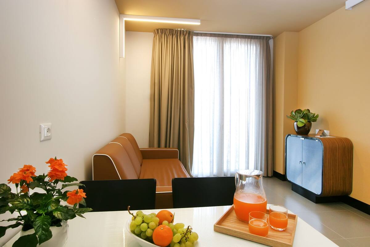 Quarto de hotel com mesa de jantar posta com frutas, jarra de suco de laranja e um armário.