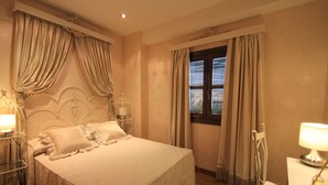 A neatly made bed with a headboard, a bedside table with a lamp, and a window with curtains. - Casa Baños de la Villa (Priego de Córdoba)