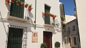 A narrow cobblestone street with white buildings, a green awning, and potted plants on balconies. - Casa Baños de la Villa (Priego de Córdoba)