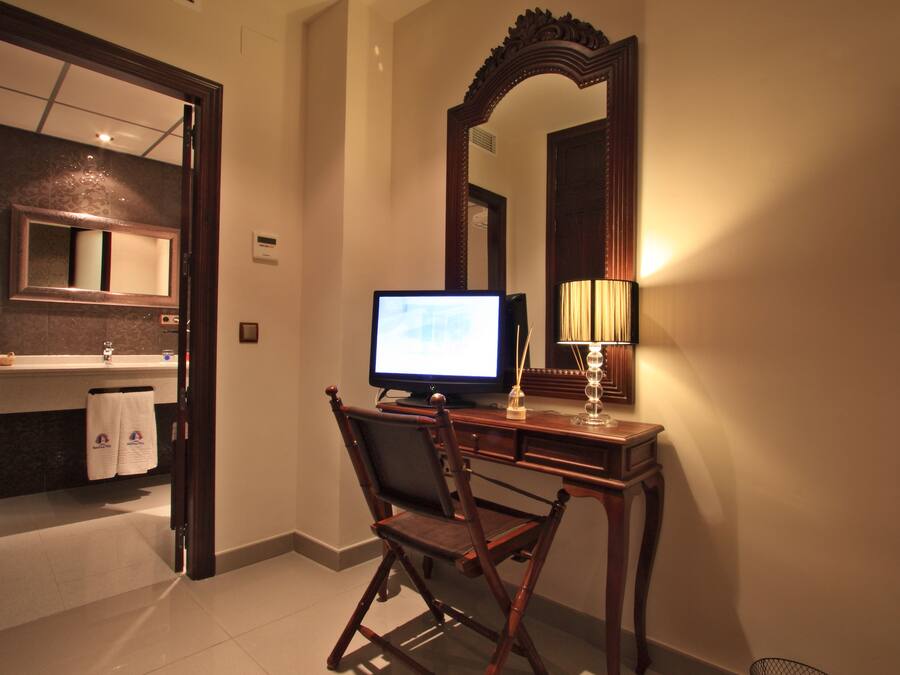 A hotel room with a desk, chair, computer, and a large mirror.