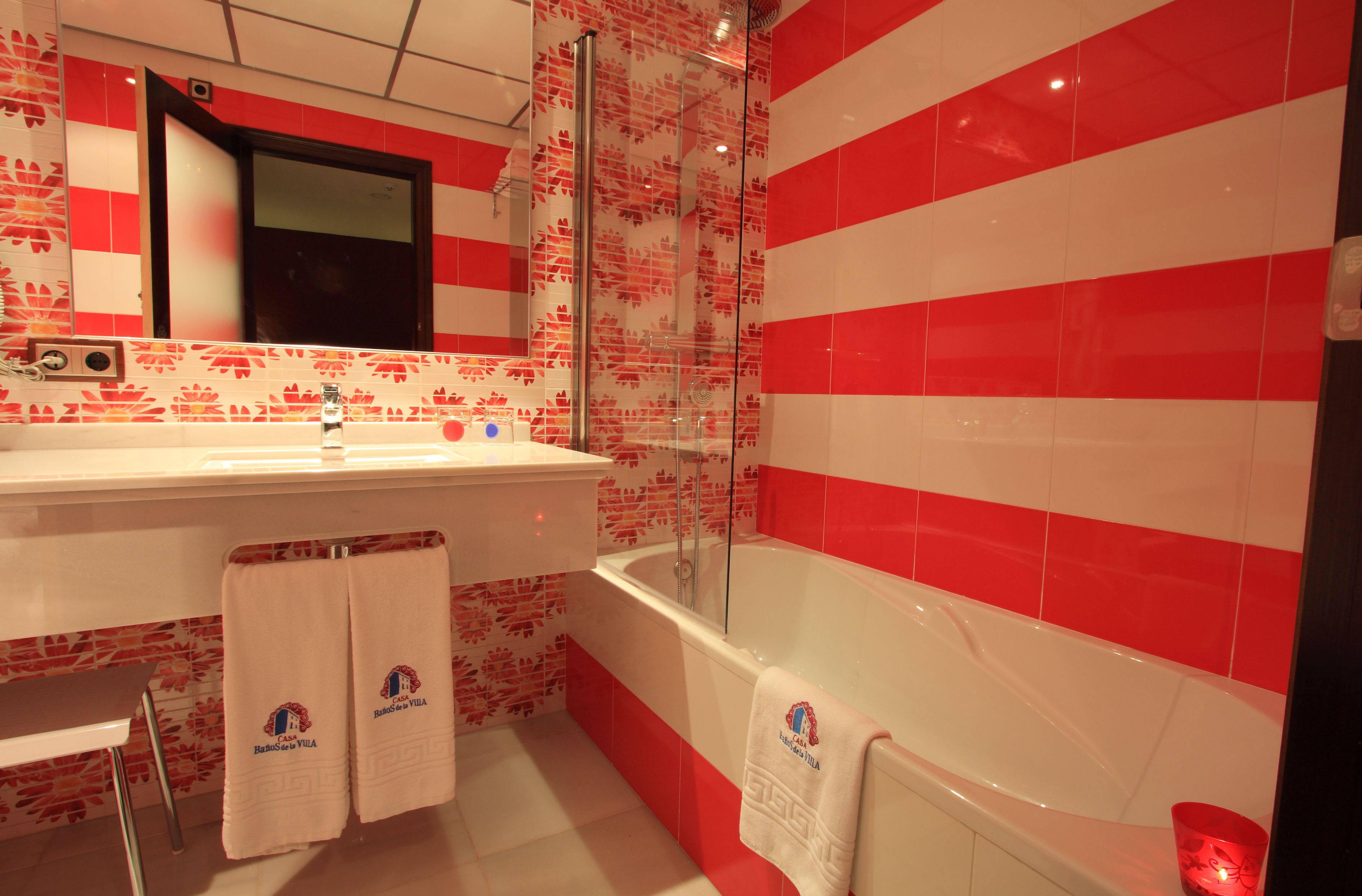 Un baño con pared de azulejos rojos y blancos, una bañera, un lavamanos y un espejo.