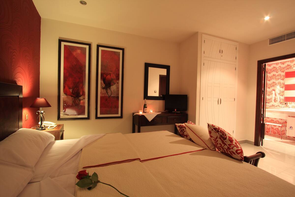 Ein Hotelzimmer mit einem Bett, einem Schreibtisch mit Lampe, einem Fernseher und zwei gerahmten Kunstwerken an der Wand.