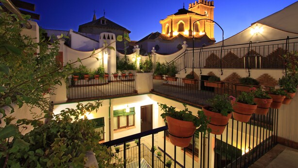 A courtyard with potted plants, a staircase, and a building with a bell tower. - Casa Baños de la Villa (Priego de Córdoba)