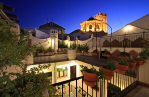 A courtyard with potted plants, a staircase, and a building with a bell tower. - Casa Baños de la Villa (Priego de Córdoba)