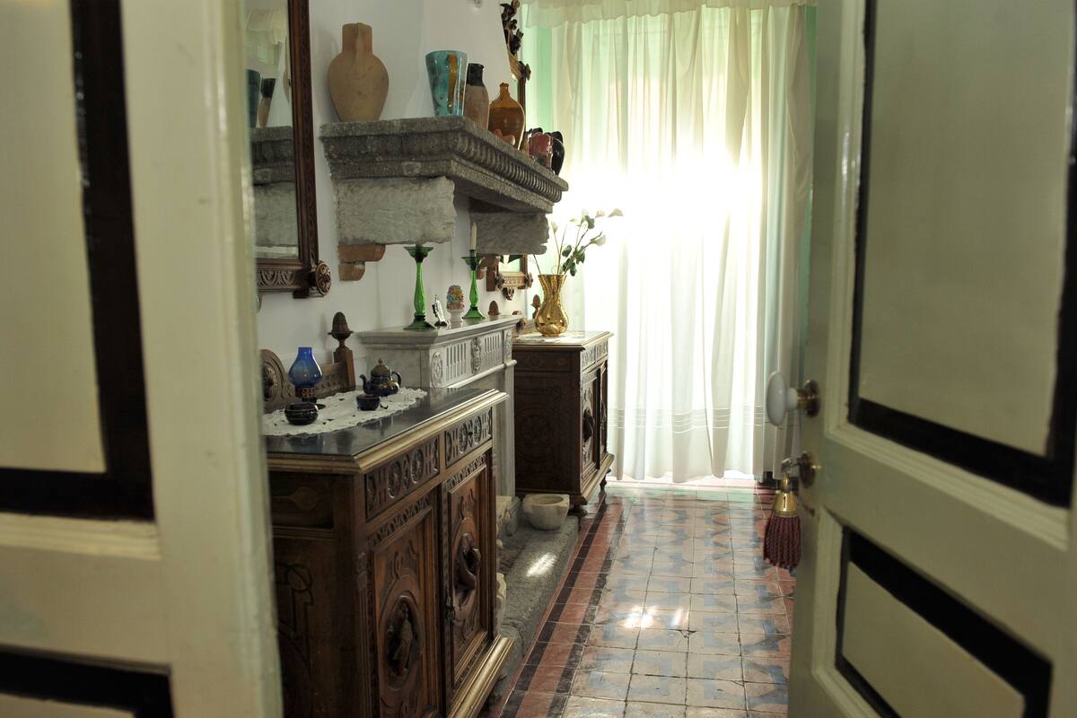 A hallway with a tiled floor, a wooden cabinet with decorative items, and a mirror on the wall.
