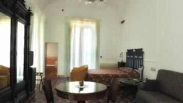 Um quarto com cama, sofá, mesa e cadeiras, espelho e um candelabro.